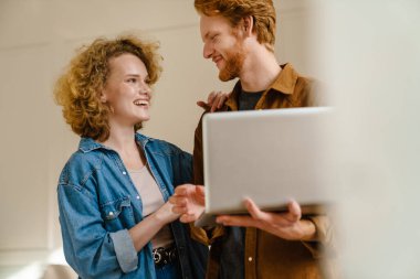 Çekici genç çift evde dikilirken dizüstü bilgisayar kullanıyor.