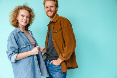 Genç mutlu kızıl saçlı çift gülümsüyor ve mavi arka planda izole edilmiş kameraya bakıyor.