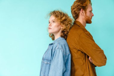 Karşıt taraflara bakan güzel kızıl saçlı çift mavi arka planda izole bir şekilde sırt sırta poz veriyor.