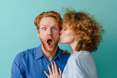 Güzel genç bir çift mavi arka planda yalnız bir yanaktan öpüşüyor.