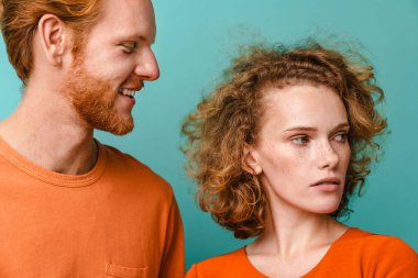 Genç ve mutlu kızıl saçlı çift mavi arka planda yalnız kalıp poz veriyorlar.