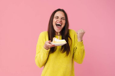 Pembe arka planda saklanmış doğum günü pastasıyla poz veren heyecanlı kız.