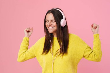 Pembe arka planda izole edilmiş kulaklıklarla müzik dinleyen neşeli, hoş bir kız.