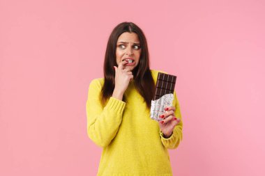 Pembe arka planda çikolata tutarken yüzünü buruşturan korkmuş güzel kız.