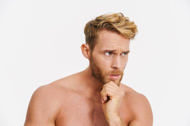 Beyaz arka planda yalnız bırakılmış beyaz gömleksiz bir adamın poz verdiğini ve ona baktığını düşünüyor.