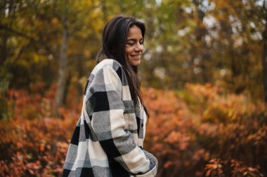Güzel esmer, mutlu kadın gülerek sonbahar ormanlarında geziniyor.