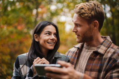Güz ormanlarında gezinirken cep telefonu kullanan ve sarılan güzel mutlu bir çift.
