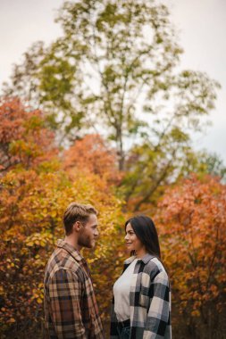 Güzel mutlu çift gülerek birbirlerini arıyorlar sonbahar ormanlarında gezinirken