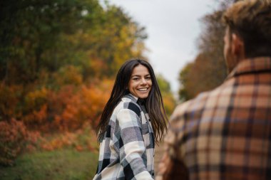 Güz ormanlarında gezinirken gülümseyen ve el ele tutuşan güzel bir çift.