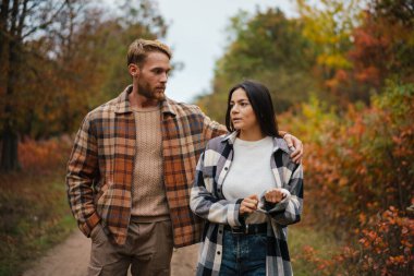 Güzel, ciddi bir çift, sonbahar ormanlarında gezinirken konuşuyor ve sarılıyorlar.