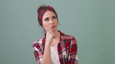 A serious young woman is thinking about something standing isolated over a green background in the studio
