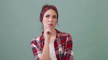 A pleased young woman is thinking about something and coming-up with an idea standing isolated over a green background in the studio