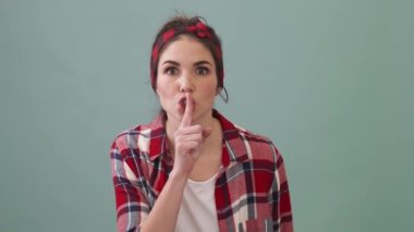 A serious woman is showing silence gesture standing isolated over a green background in the studio