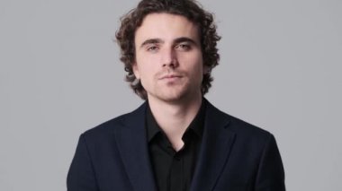 A serious young man is showing thumb-down gesture standing isolated over gray wall in the studio
