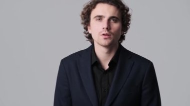 A shocked nervous young man is hiding his face with his hands standing isolated over gray wall in the studio