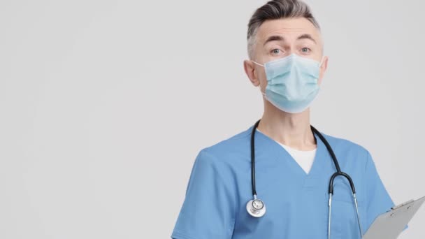 Przystojny Starszy Lekarz Mundurze Medycznym Wskazuje Bok Odizolowany Szarym Tle — Wideo stockowe