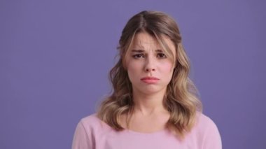 A sad woman is looking to the camera standing isolated over a violet background