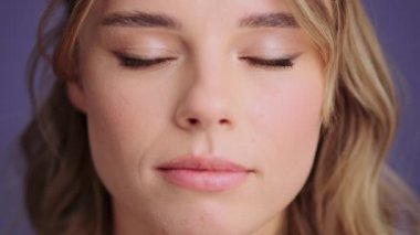 A beautiful young woman is opening her eyes and looking to the camera standing isolated over gray wall in the studio