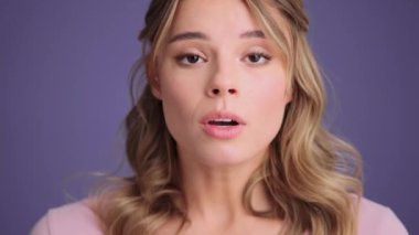 A close-up view of a shocked young woman is looking to the camera standing isolated over gray wall in the studio