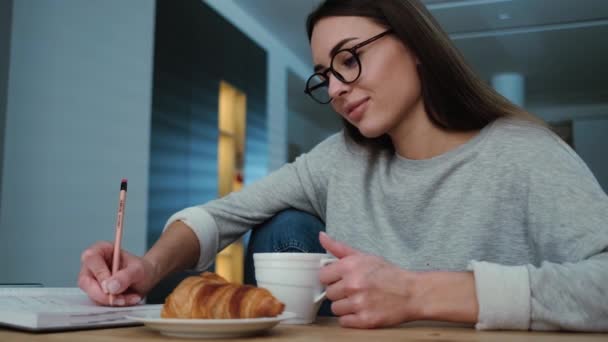 Een Aantrekkelijke Jonge Vrouw Schrijft Iets Terwijl Croissants Eet Appartementen — Stockvideo