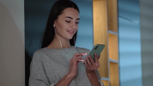 Щаслива Жінка Навушниках Використовує Свій Смартфон Стоїть Всередині Квартири — стокове відео