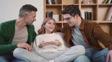 Joyful gay family are using mobile phone while sitting on couch at home