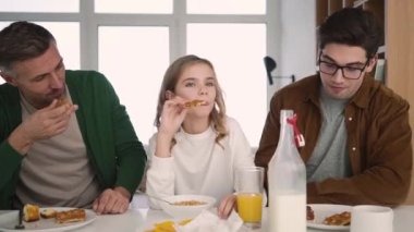 Happy gay family are talking while having breakfast in the kitchen at home