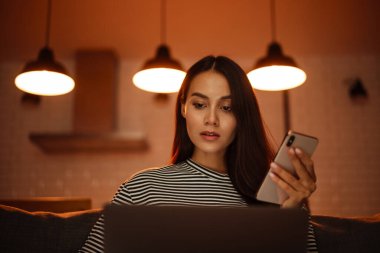 Evdeki kanepede dizüstü bilgisayarla çalışırken cep telefonu kullanan çok güzel bir kadın.