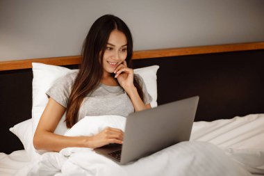 Evde yatarken dizüstü bilgisayarla çalışan neşeli güzel bir kadın.