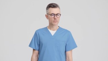 A thinking doctor man wearing uniform is raising his finger while coming-up with an idea standing isolated over grey background in the studio