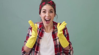 A happy cleaner woman is rejoicing while clapping her hands standing isolated over a green background in the studio