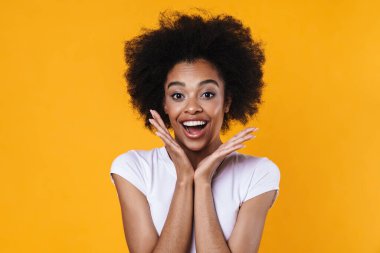 Heyecanlı Afrikalı Amerikalı kız sarı arka planda izole edilmiş kameraya şaşırdığını ifade ediyor.