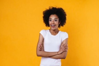 Heyecanlı Afrikalı Amerikalı kız, sarı arka planda kollarını kavuşturup poz veriyor.