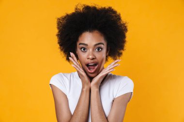 Şok olmuş Afrikalı Amerikalı kız sarı arka planda izole edilmiş kameraya şaşırdığını ifade ediyor.