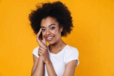 Mutlu Afrikalı Amerikalı kız gülümsüyor ve sarı arka planda izole edilmiş kameraya bakıyor.