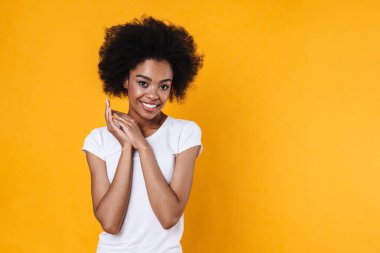 Mutlu Afrikalı Amerikalı kız gülümsüyor ve sarı arka planda izole edilmiş kameraya bakıyor.