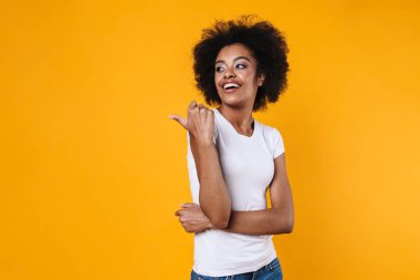 Mutlu Afrikalı Amerikalı kız gülümsüyor ve sarı arka planda izole edilmiş kopyalama alanını işaret ediyor.