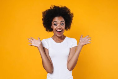 Heyecanlı Afrikalı Amerikalı kız şaşırdığını ve sarı arka planda izole bir şekilde kollarını hareket ettirdiğini ifade ediyor.