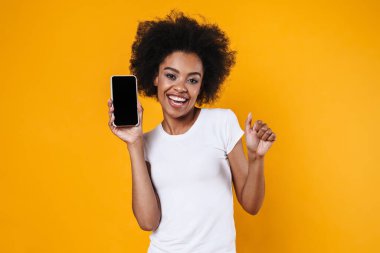 Sarı arka planda cep telefonuyla gülümseyen mutlu Afrikalı genç Amerikalı kadın.