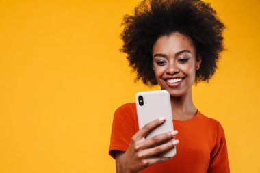 Sarı arka planda izole edilmiş cep telefonu kullanırken gülümseyen Afrikalı Amerikalı kız.