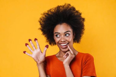 Gülümseyen Afrikalı Amerikalı kız sarı arka planda saklanmış ahududularıyla dalga geçiyor.