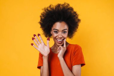 Gülümseyen Afrikalı Amerikalı kız sarı arka planda saklanmış ahududularıyla dalga geçiyor.