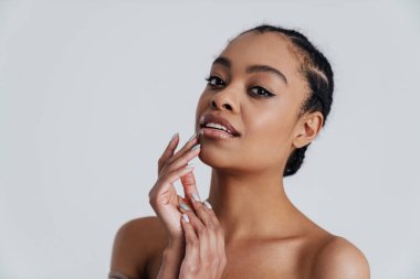 Beyaz arka planda yalnız bırakılmış, poz veren ve kameraya bakan Afro-Amerikan kadın.