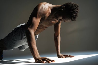 Gri arka planda izole edilmiş bir spor minderi üzerinde egzersiz yapan kendinden emin genç Afrikalı sporcu.