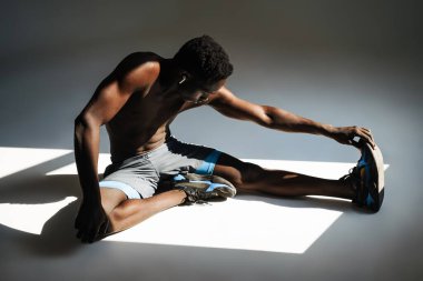 Kendine güvenen Afrikalı sporcu gri arka planda izole edilmiş bir spor minderi üzerinde egzersiz yapıyor.