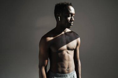 Arkaplanda kablosuz kulaklık kullanarak izole bir şekilde duran kaslı, formasız, yakışıklı bir sporcunun portresini yakından çek.