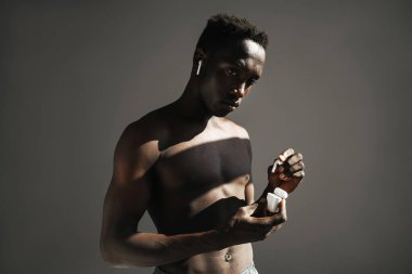 Arkaplanda kablosuz kulaklık kullanarak izole bir şekilde duran kaslı, formasız, yakışıklı bir sporcunun portresini yakından çek.