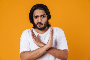 Üzgün genç Hintli adam sarı arka planda izole edilmiş inkar jesti gösteriyor.