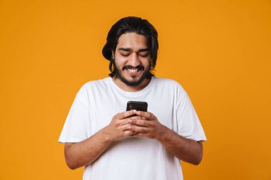 Sarı arka planda izole edilmiş cep telefonu kullanan mutlu Hintli genç adam.