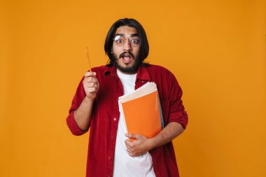 Sarı arka planda izole edilmiş ders kitaplarını tutan heyecanlı Hintli genç adam.
